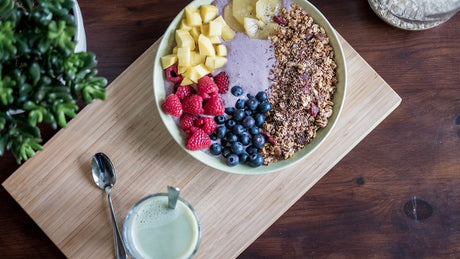 Smoothie bowl topped with granola, berries, mango, and kiwi beside a green drink